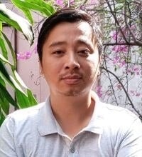 Portrait of a man with light facial hair standing outdoors near green plants and flowers