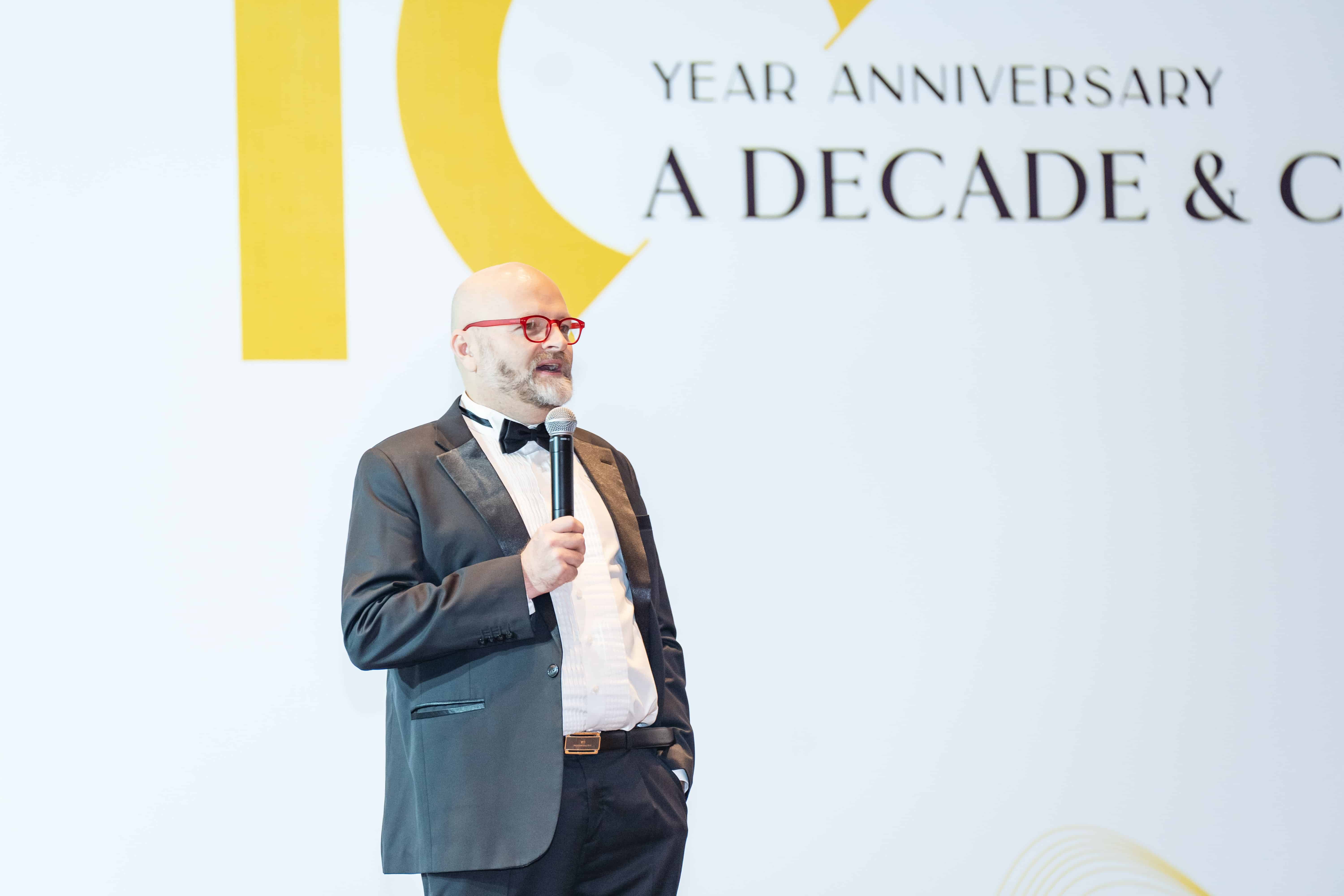 Man in tuxedo giving speech at 10-year anniversary celebration event