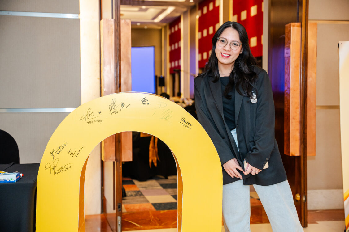 Smiling woman in business casual outfit with signed yellow event prop