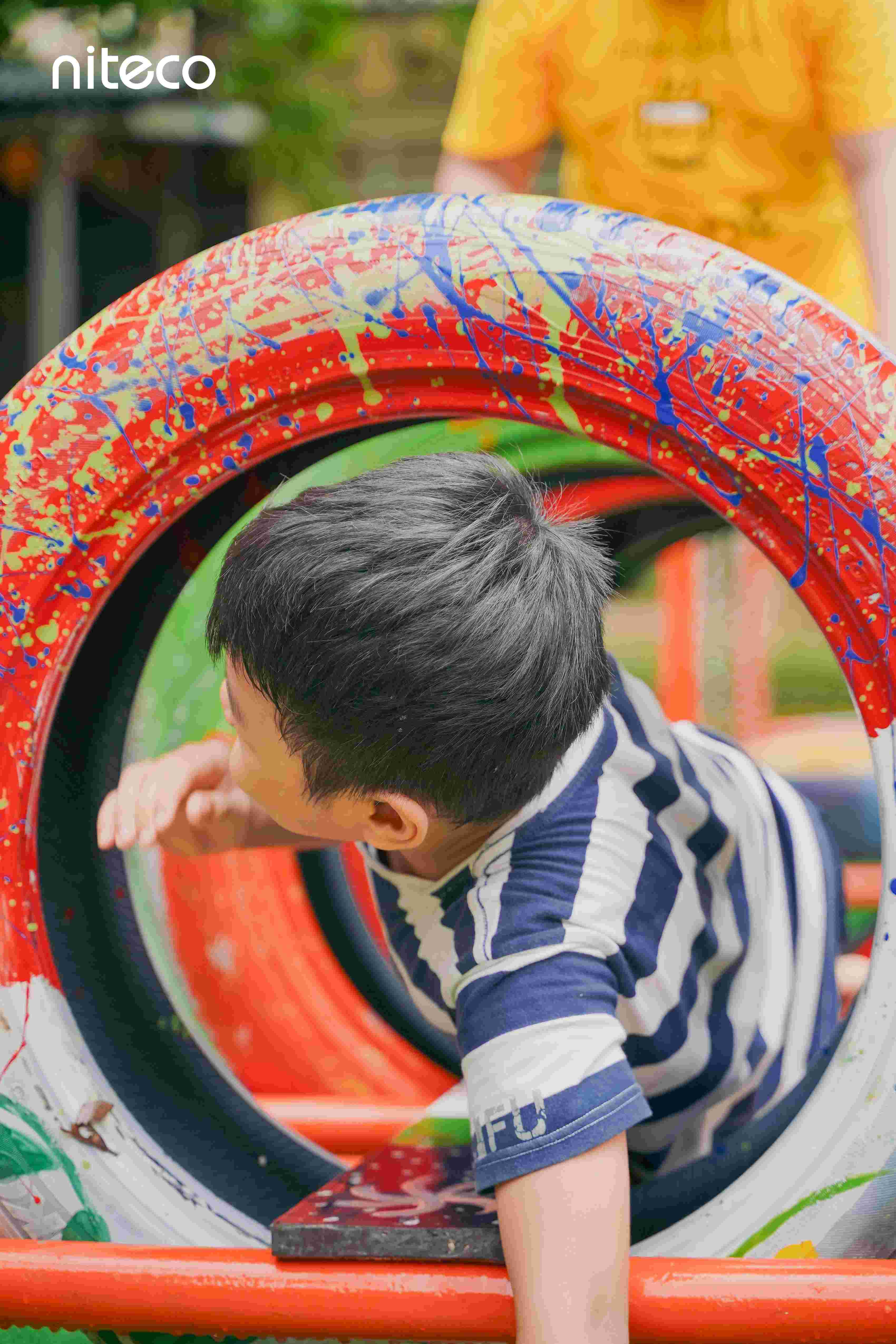 Child playing in colorful tires on playground with Niteco logo visible