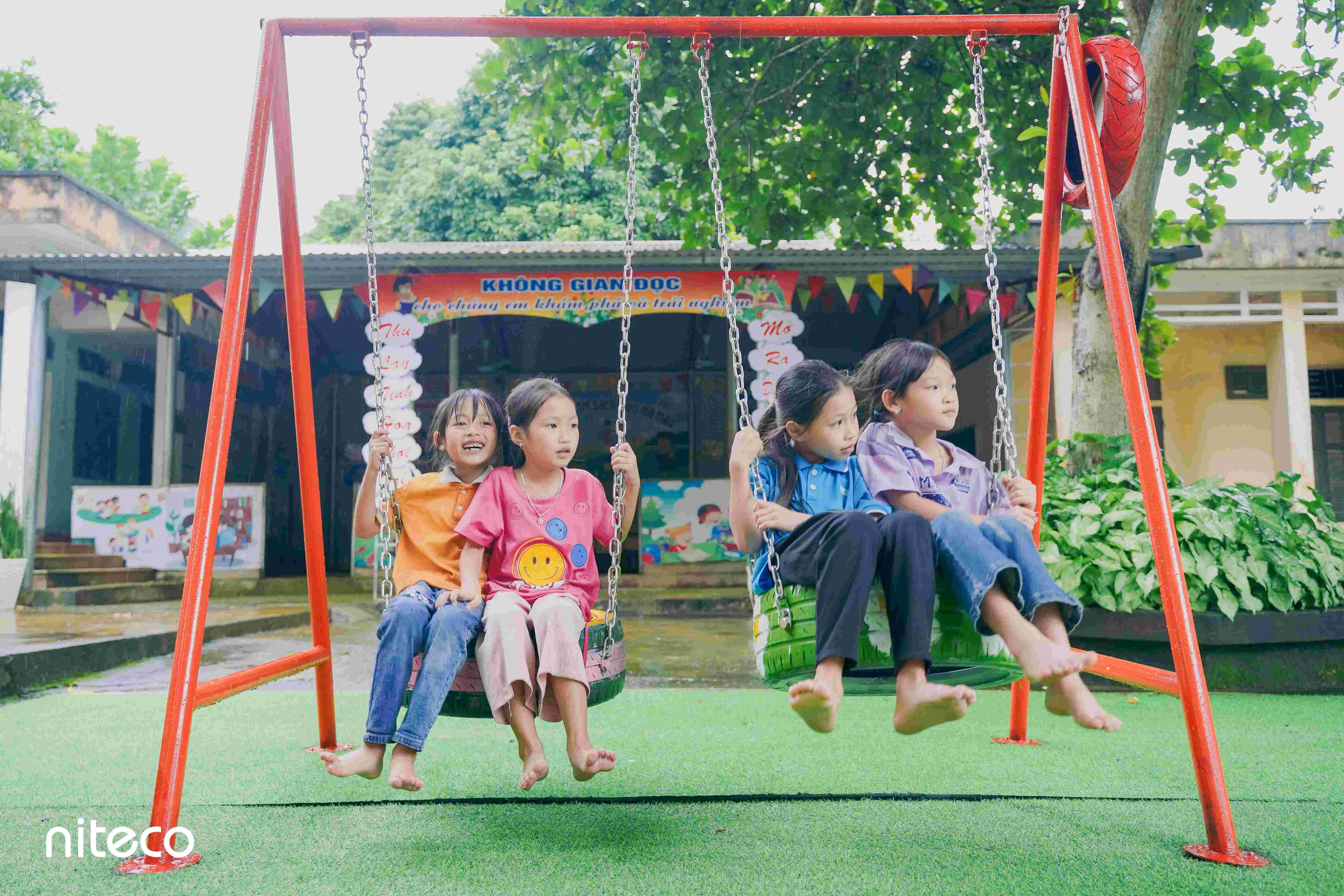 Four children playing on tire swings in a colorful outdoor playground environment