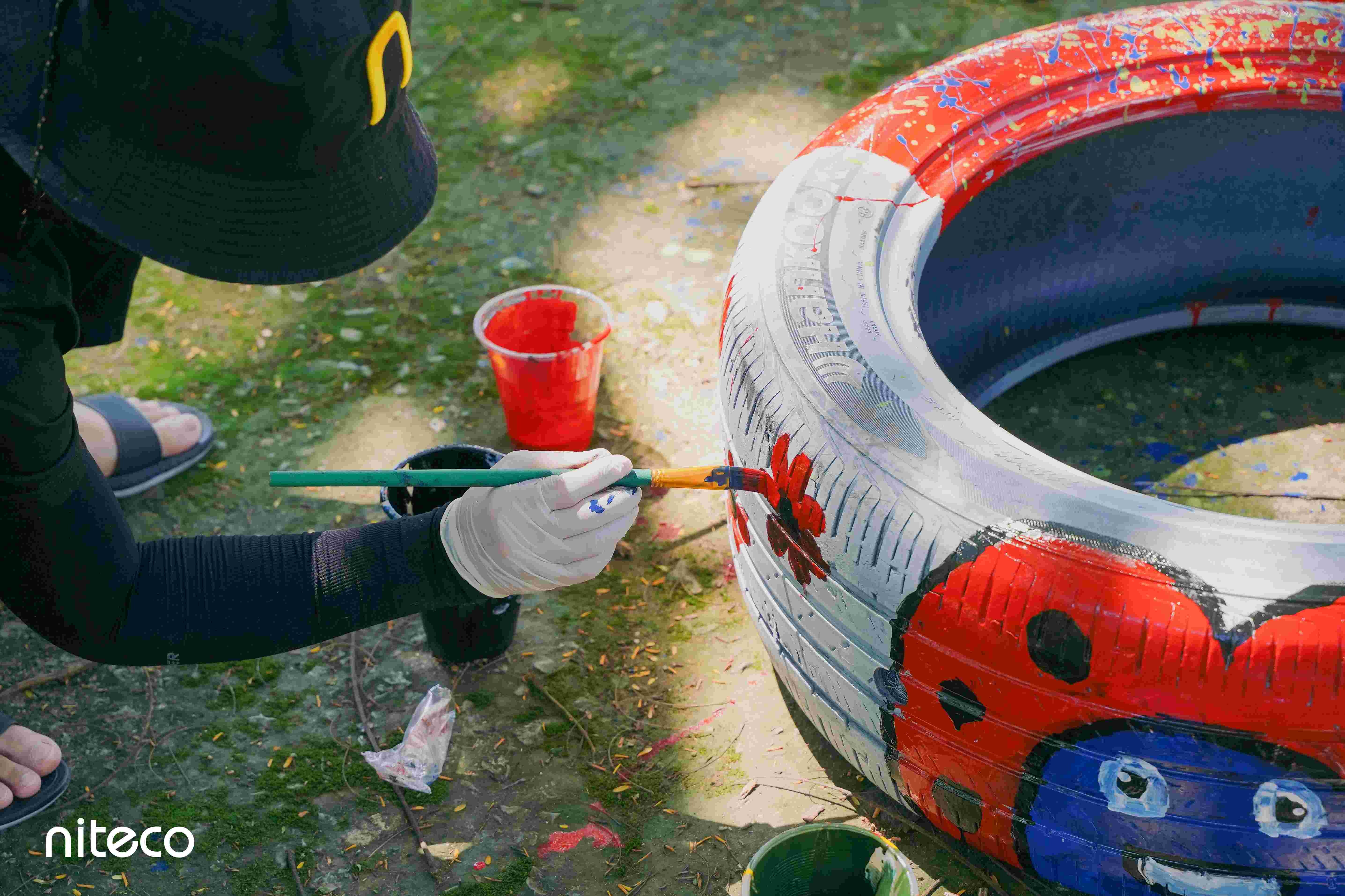 Person painting red flowers on white tire for outdoor upcycling project
