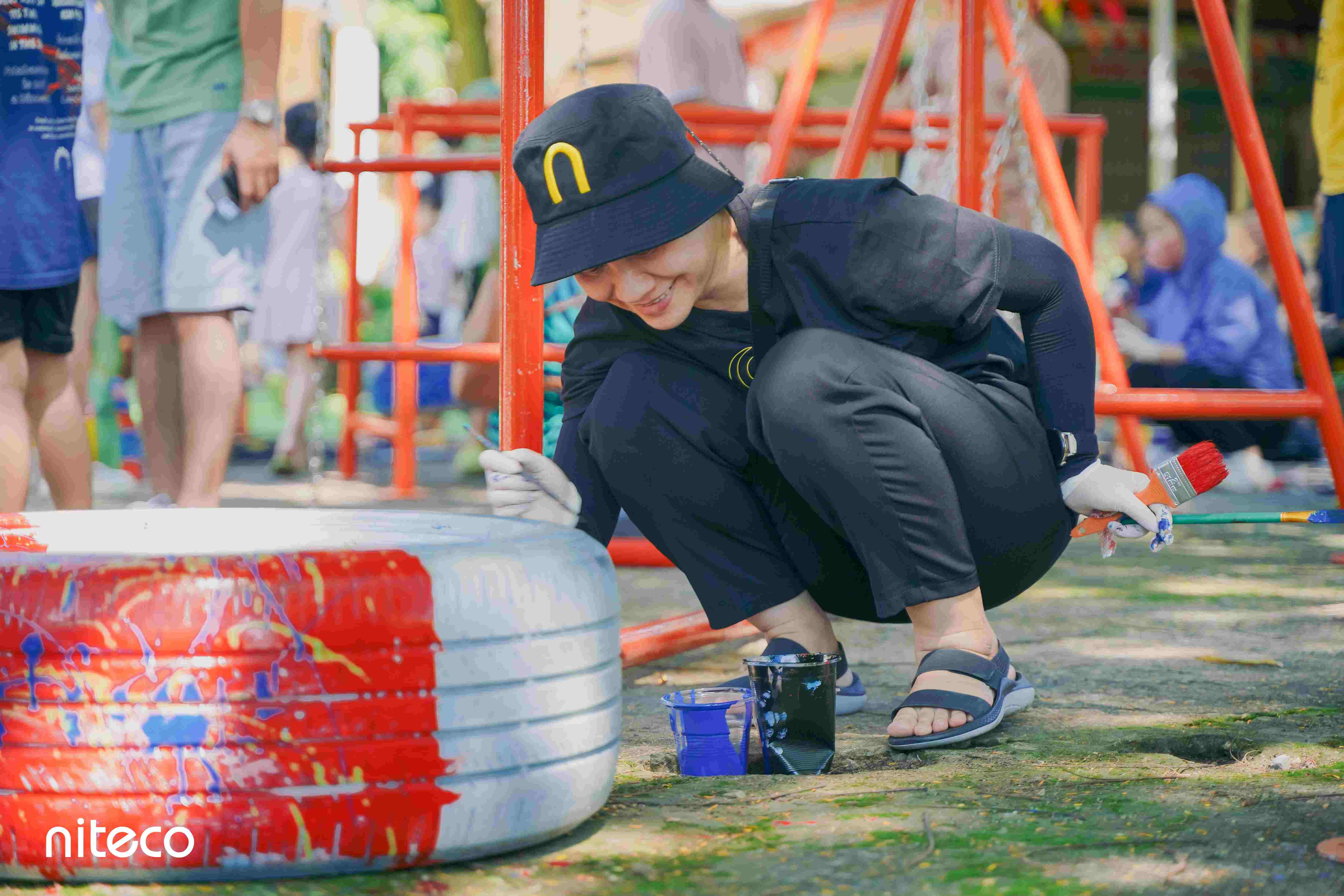 Person painting old tire red and white for playground recycling project