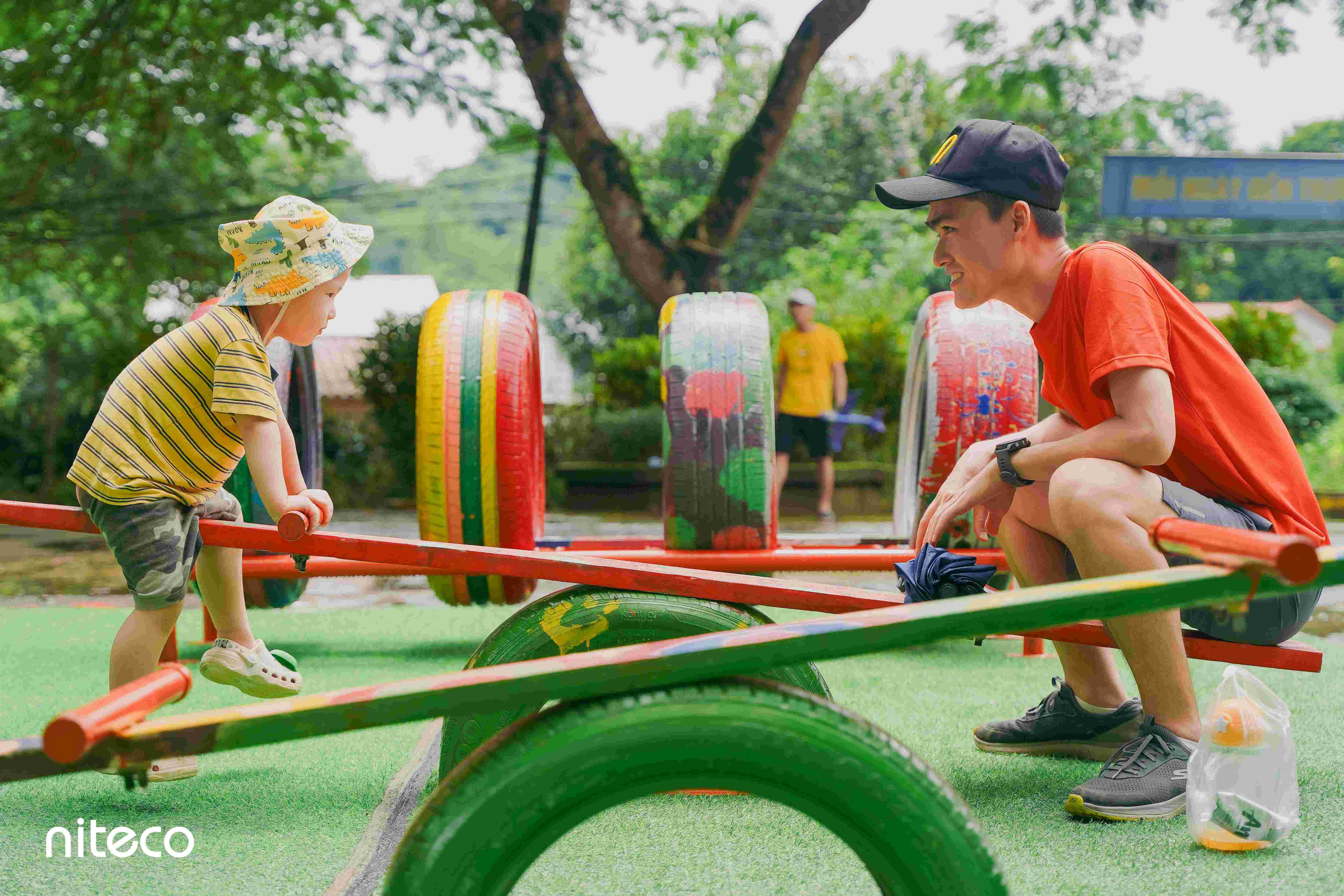Child and adult playing on colorful seesaw in outdoor playground with tires