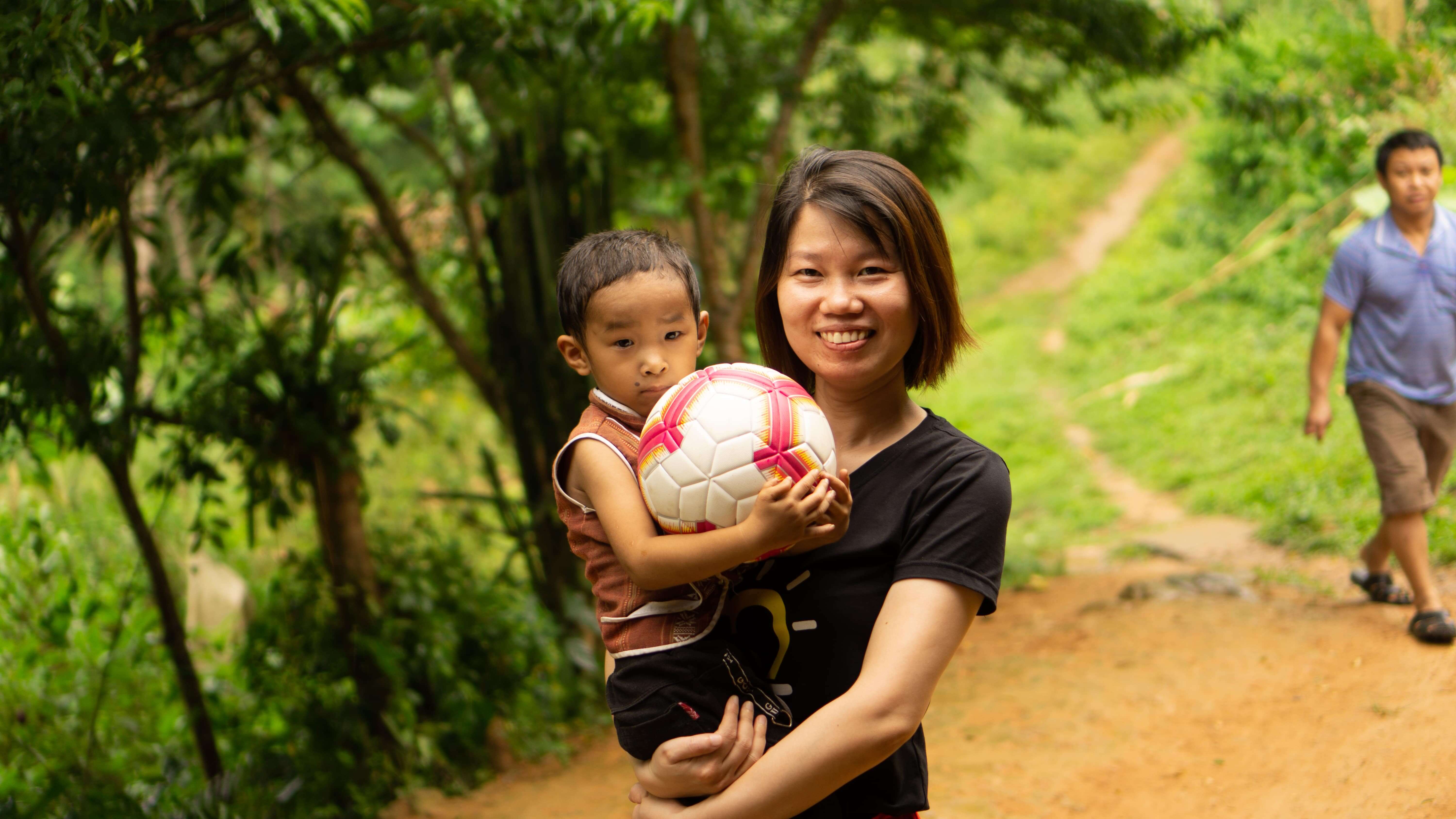 Woman holding child with soccer ball on rural trail with greenery
