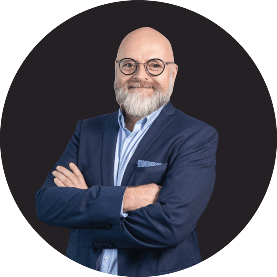 Mature bald man with beard and glasses wearing navy suit smiling.