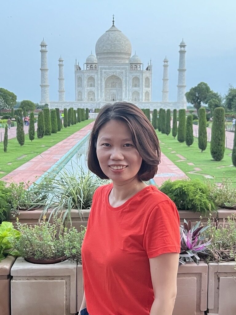 Woman in red shirt smiling with the Taj Mahal and garden in the background