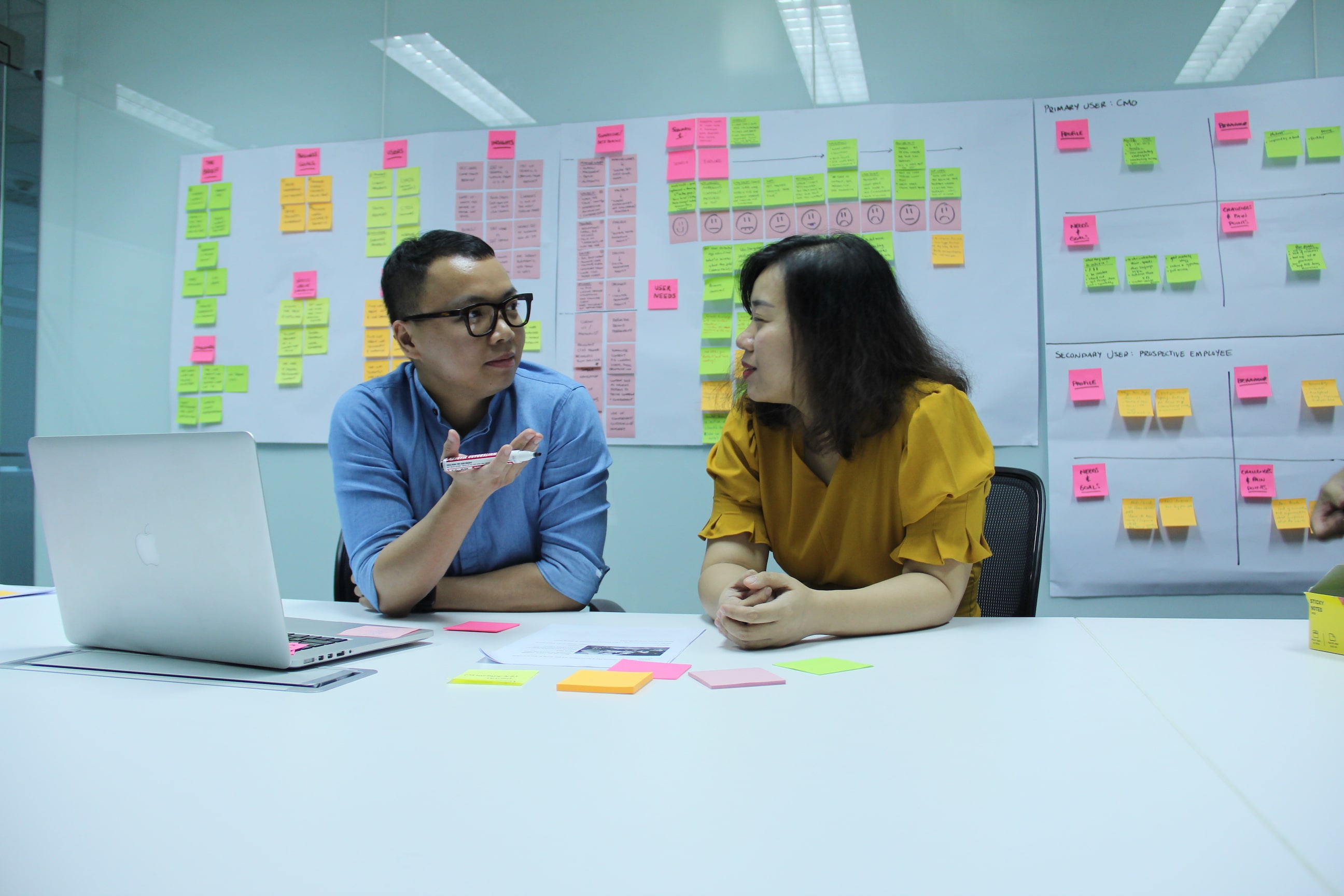 Two colleagues discussing project planning with sticky notes and laptop in office