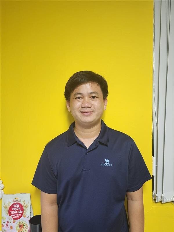 Man wearing navy polo with camel logo standing against yellow wall