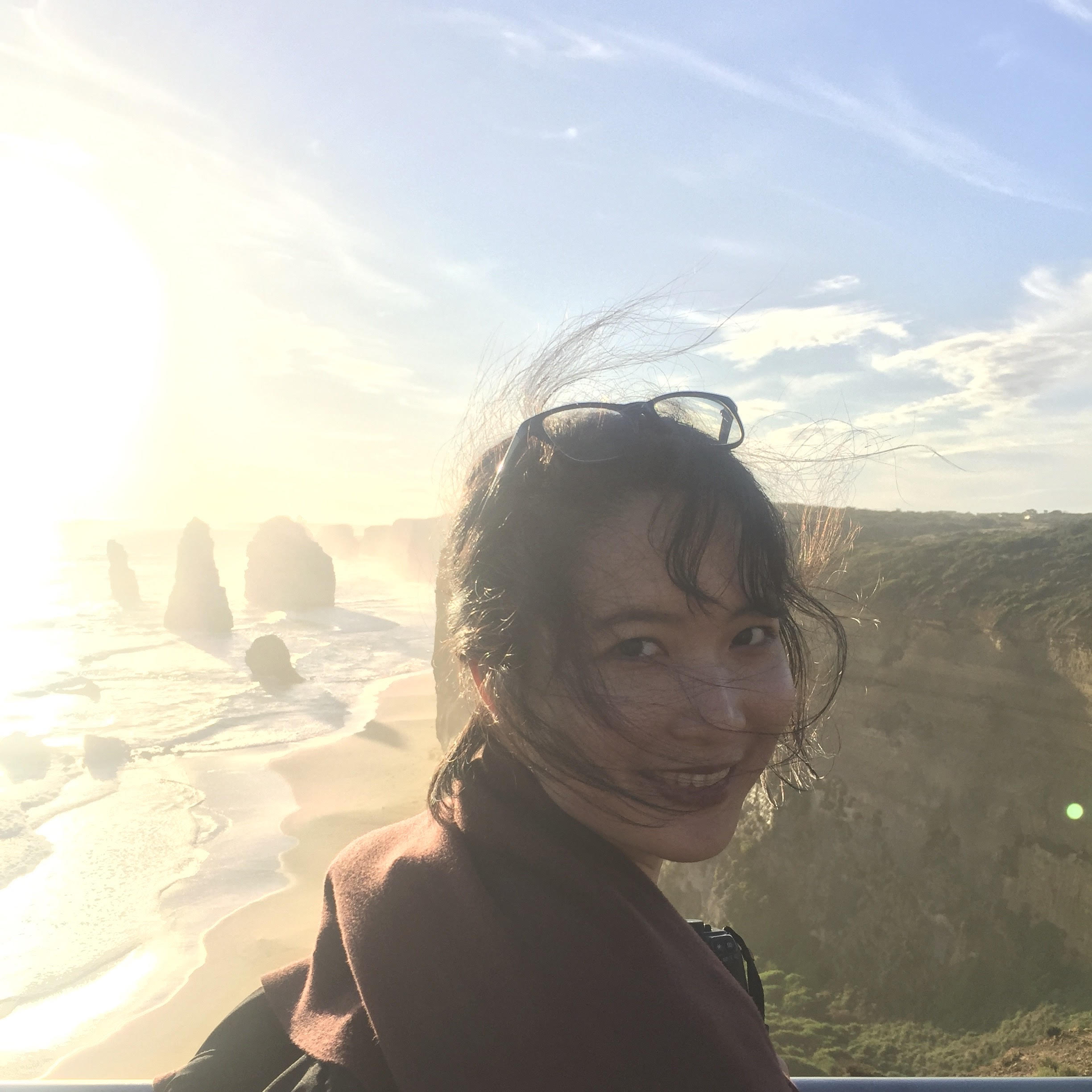 Woman smiling with sunglasses on head at Twelve Apostles coastal rock formations