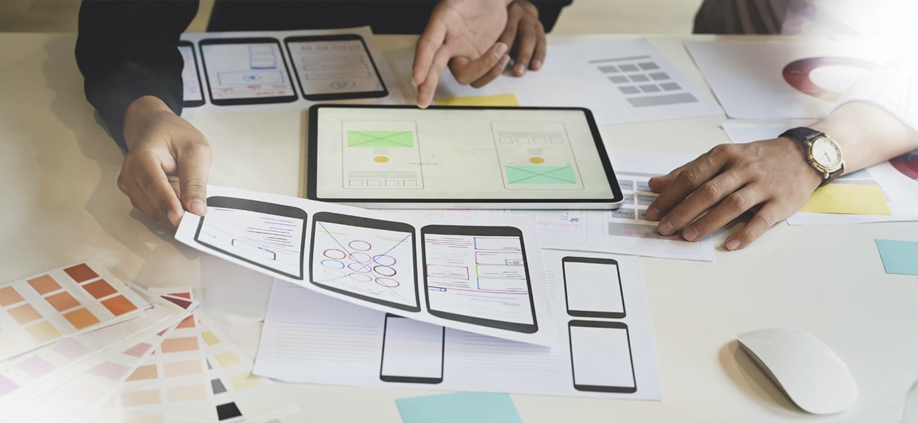 Hands working on UX design wireframes and color palettes on a desk