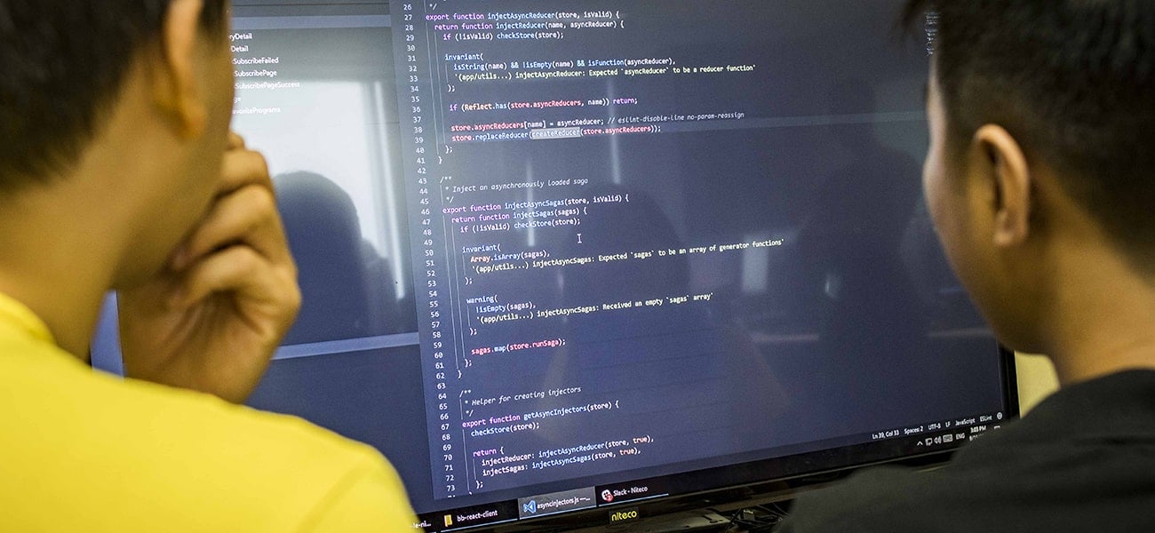 Two software developers reviewing asynchronous JavaScript code on monitor
