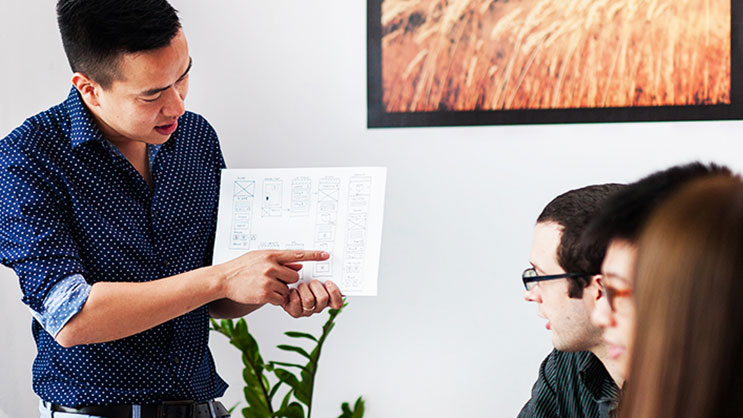 Man presenting wireframe design to colleagues during UX design meeting
