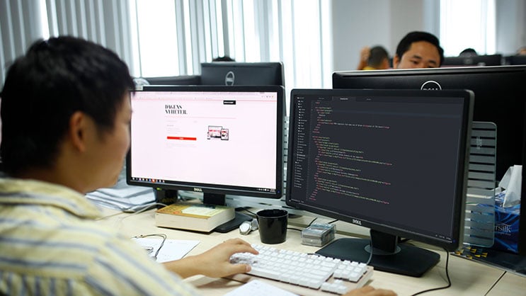 Developer coding website on dual monitors in modern office workspace