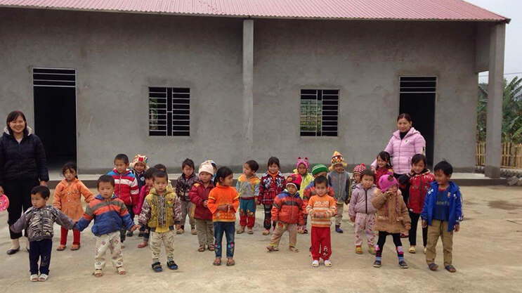 Children and teachers standing outside a rural kindergarten building in Vietnam