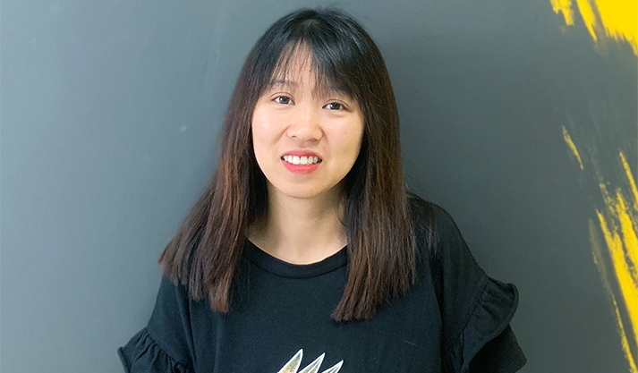 Smiling woman with straight dark hair wearing black shirt against gray wall