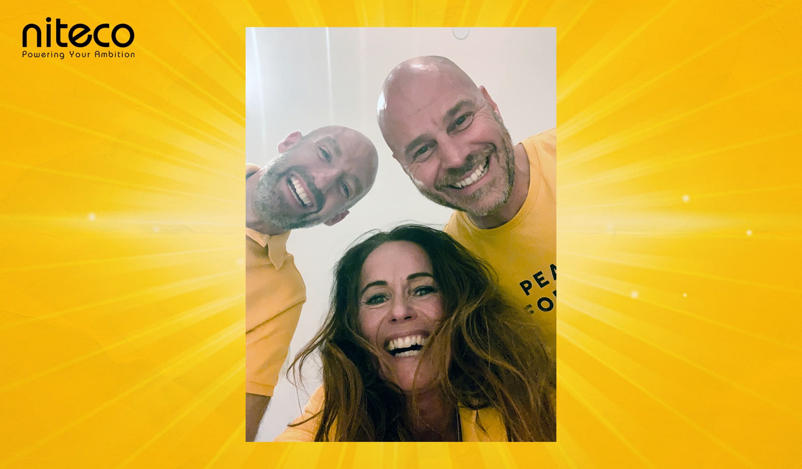 Three smiling team members wearing yellow shirts with Niteco logo background